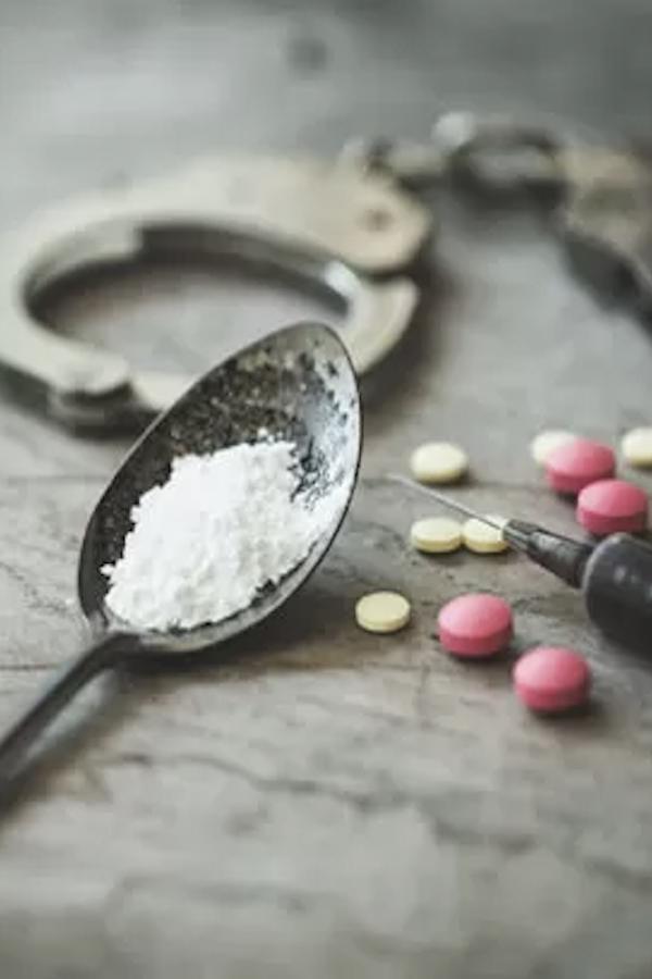 a spoon, a syringe, handcuffs and some pills over a table